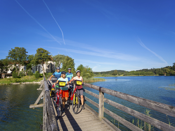 Radfahrer auf Holzbrücke am Chiemsee bei sonnigem Wetter.