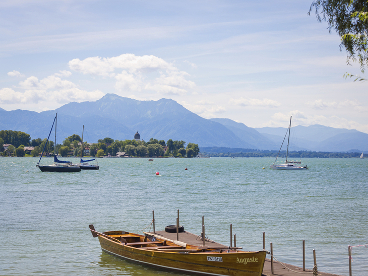 Bootsanleger am Chiemsee mit Segelbooten und Bergen im Hintergrund.
