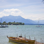 Bootsanleger am Chiemsee mit Segelbooten und Bergen im Hintergrund.