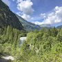 Berglandschaft mit Fluss und bewaldeten Hügeln unter blauem Himmel.