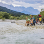 Personen mit Fahrrädern am Flussufer, Berge im Hintergrund
