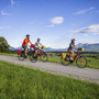 Radfahrer auf dem Lechradweg vor Alpenkulisse bei sonnigem Wetter.