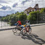 Zwei Radfahrer auf einer Brücke in Füssen, mit historischen Gebäuden im Hintergrund.