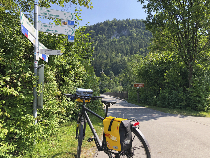 Fahrrad am Wegweiser auf dem Lechradweg in grüner Berglandschaft.