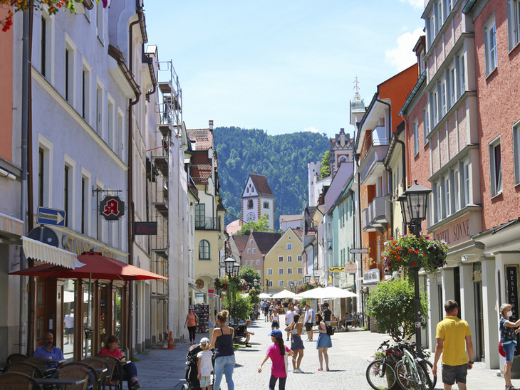 Fußgängerzone in Füssen mit Alpen im Hintergrund bei sonnigem Wetter.