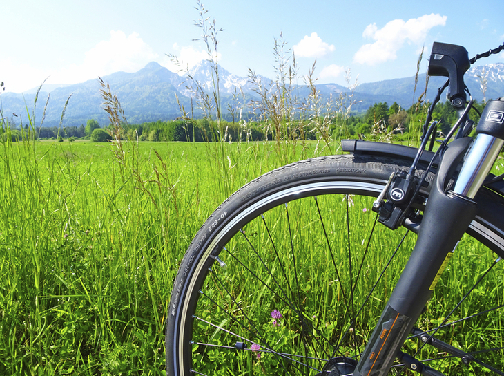 Fahrrad vor grüner Wiese mit Bergen im Hintergrund unter blauem Himmel