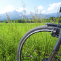 Fahrrad vor grüner Wiese mit Bergen im Hintergrund unter blauem Himmel