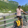 Radfahrerin auf Brücke über Fluss, umgeben von Wald und Berglandschaft.