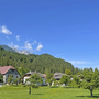 Mehrere Häuser vor bewaldeten Bergen und blauem Himmel.