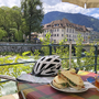 Fahrradhelm und Panini auf Tisch mit Fluss und Bergen im Hintergrund.