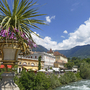 Blick auf Fluss und Gebäude in Meran mit Blumen im Vordergrund.