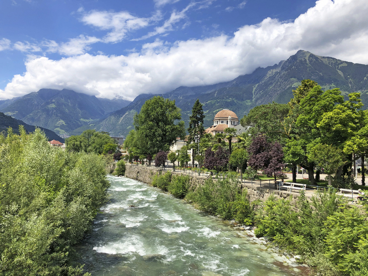 Fluss in Südtirol mit Bergen und üppiger Vegetation im Hintergrund.