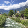 Fluss in Südtirol mit Bergen und üppiger Vegetation im Hintergrund.