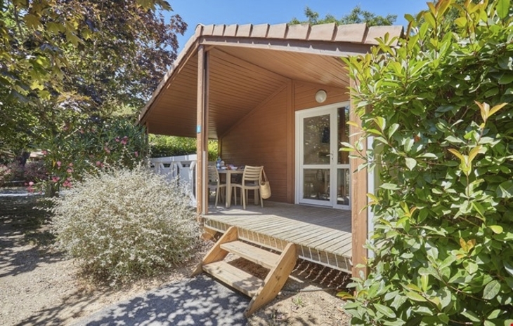 Kleine Holzveranda mit Tisch und Stühlen, umgeben von grüner Vegetation.