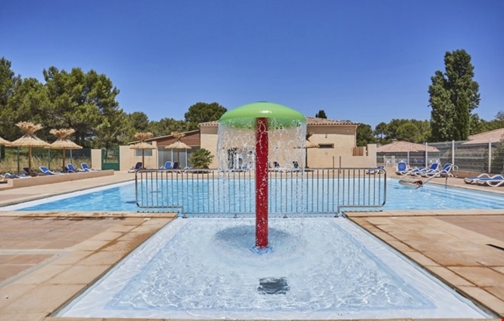 Poolbereich mit Wasserfontäne, umgeben von Liegestühlen und Sonnenschirmen