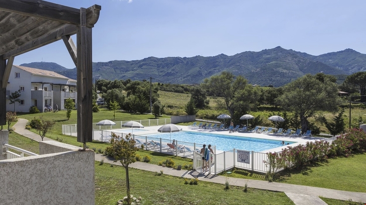 Blick auf einen Pool vor Bergen und Grünflächen bei einer Ferienresidenz.