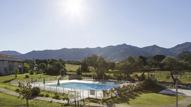 Außenpool mit Liegestühlen, umgeben von Landschaft und Bergen bei Sonnenschein.