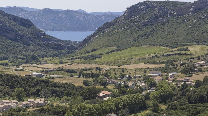 Blick auf ein Tal mit mediterraner Landschaft und einem Dorf, Berge im Hintergrund.