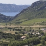 Blick auf ein Tal mit mediterraner Landschaft und einem Dorf, Berge im Hintergrund.
