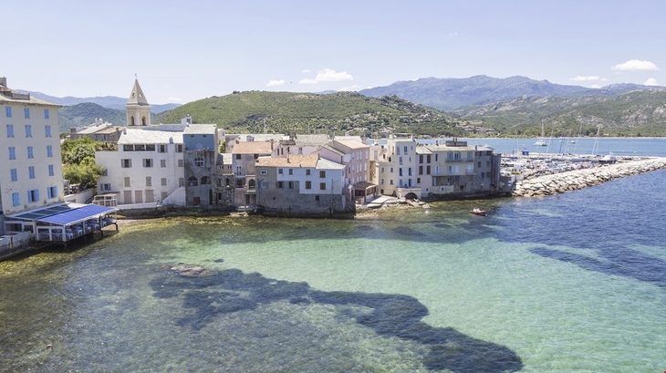 Küstenstadt mit Gebäuden am Meer und Bergen im Hintergrund in Saint-Florent, Korsika.