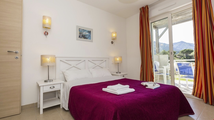 Schlafzimmer in einer Ferienwohnung mit Doppelbett und Zugang zu einem Balkon.