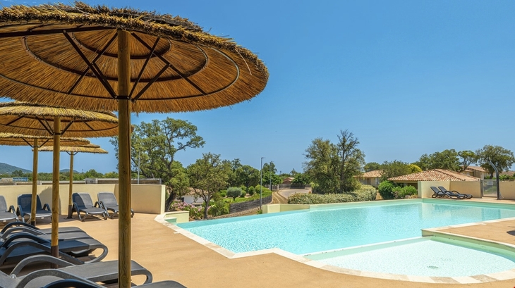 Pool mit Liegestühlen und Sonnenschirmen in einer sonnigen Umgebung