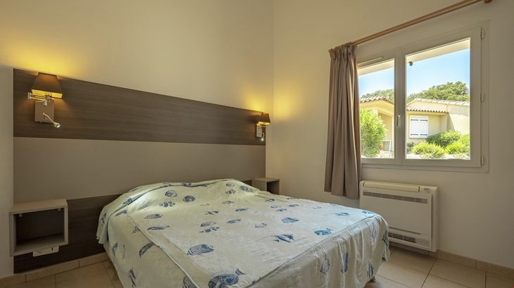 Helles Schlafzimmer mit Doppelbett, Wandlampen und Blick aus dem Fenster ins Freie.