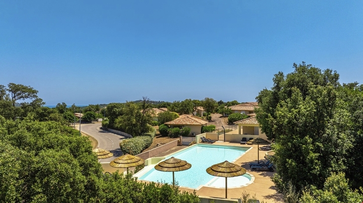 Resort mit Pool und Sonnenschirmen in einer grünen Umgebung.
