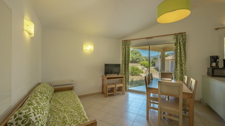 Wohnzimmer mit Sofa, Esstisch, TV und Blick auf eine Terrasse.