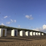 Strandhütten an einem sonnigen Sandstrand mit blauem Himmel und Wolken.