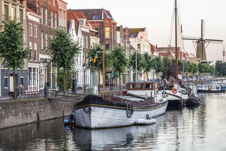 Boote am Kanal vor historischen Gebäuden und einer Windmühle in Rotterdam.