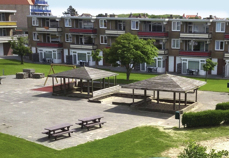 Ferienanlage mit Spielplatz und Bänken vor mehrstöckigen Gebäuden.