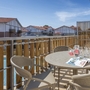 Balkon mit Tisch, Stühlen und Getränken, Blick auf Pool und Gebäude im Hintergrund.