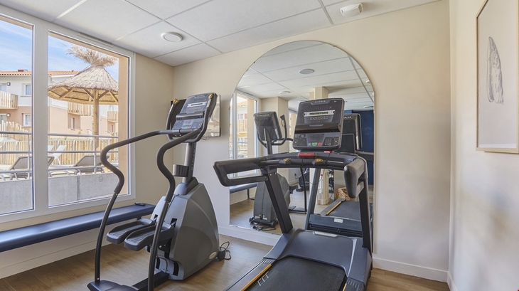 Fitnessraum mit Laufband und Crosstrainer vor einem Spiegel.