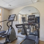 Fitnessraum mit Laufband und Crosstrainer vor einem Spiegel.
