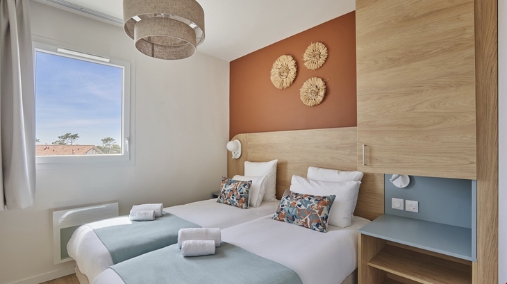 Helles Schlafzimmer mit zwei Einzelbetten, Fensterblick auf eine sonnige Landschaft.
