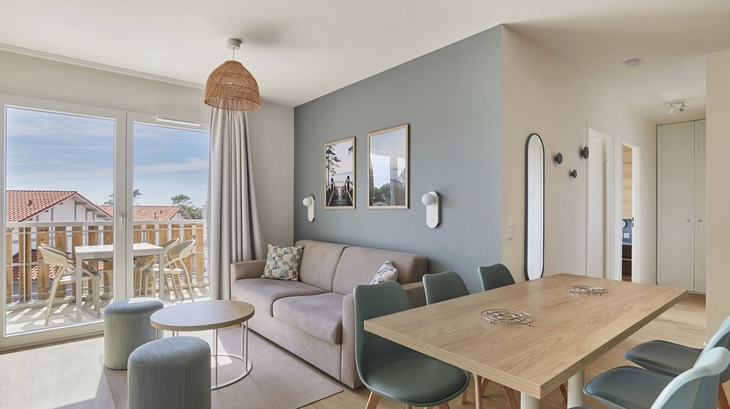 Wohnzimmer mit Sofa, Tisch, Stühlen und Zugang zu einem Balkon mit Holzmöbeln.