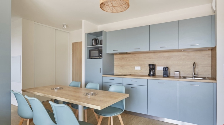Küche mit blauen Schränken, Esstisch und Stühlen in modernem Apartment.