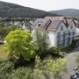 Hotel mit Solarpanels, umgeben von Bäumen und Wohnhäusern in ländlicher Umgebung.