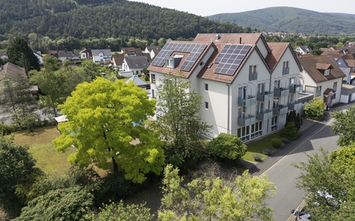 Hotel mit Solarpanels, umgeben von Bäumen und Wohnhäusern in ländlicher Umgebung.