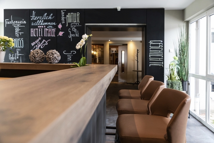 Lobby des Hotels Imhof in Gemünden mit Holztheke und Pflanzen.