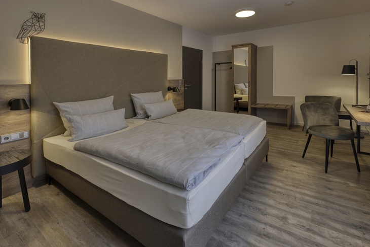 Modernes Hotelzimmer mit Doppelbett und Schreibtisch, dezente Einrichtung.