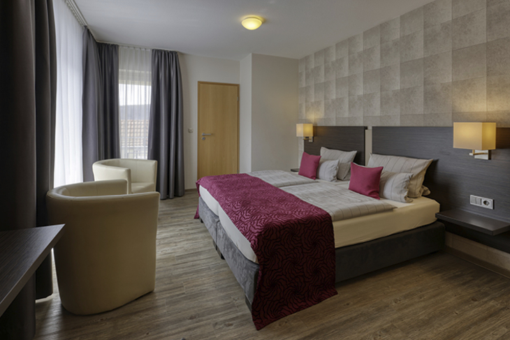 Modernes Hotelzimmer mit Doppelbett, roten Akzenten und Sitzbereich in Gemünden.