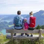 Familie auf Bank mit Wanderrucksäcken, blickt auf Berge und See im Salzkammergut.