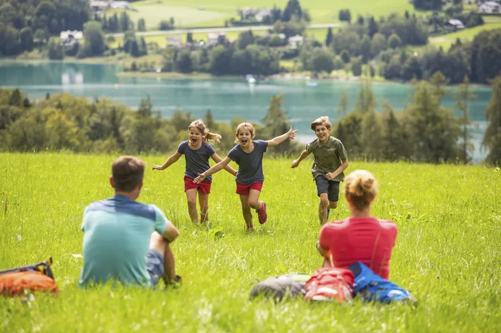 Familie rastet auf Wiese mit See im Hintergrund im Salzkammergut.