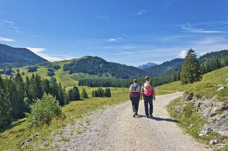 Paar wandert auf einem Weg in einer alpinen Landschaft bei sonnigem Wetter.