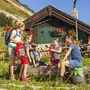 Familie rastet vor Almhütte im Salzkammergut bei sonnigem Wetter.
