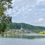 Flusslandschaft mit Dorf und Kirche im Hintergrund unter bewölktem Himmel.