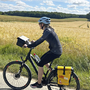 Radfahrer auf Landstraße neben Getreidefeld bei sonnigem Wetter.