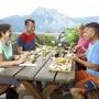 Personen essen gemeinsam an einem Holztisch mit Bergblick im Hintergrund.